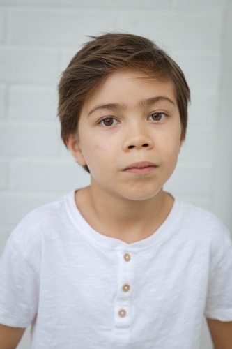 Portrait of young boy against white wall - Australian Stock Image