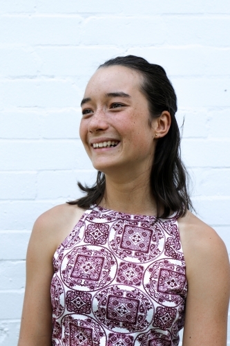 Portrait of young girl smiling in front of white brick wall - Australian Stock Image