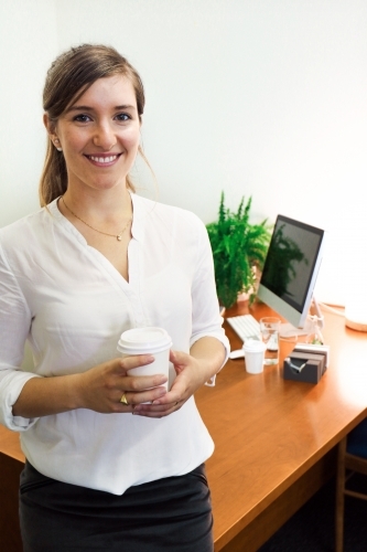 Portrait of young professional woman holding a coffee in the office - Australian Stock Image