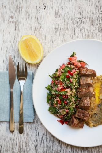 Portrait shot of a dish with beef and vegetables with a lemon, spoon, fork and napkin on the side - Australian Stock Image