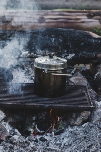 Pot cooking on grill on smoking camp fire - Australian Stock Image