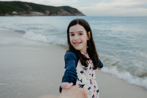 POV Of Mother holding her daughter's hand at the beach at sunset - Australian Stock Image