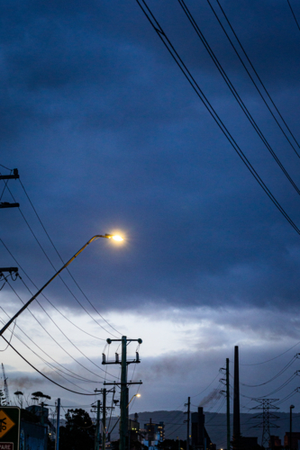 Powerlines and street light against dark clouds in sky - Australian Stock Image