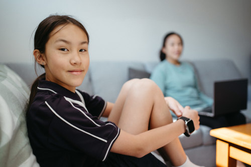 Pre-teen age girl sitting on the couch with mum on the other side - Australian Stock Image