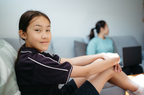 Pre-teen age girl sitting on the couch looking at the camera with mum on the other side - Australian Stock Image