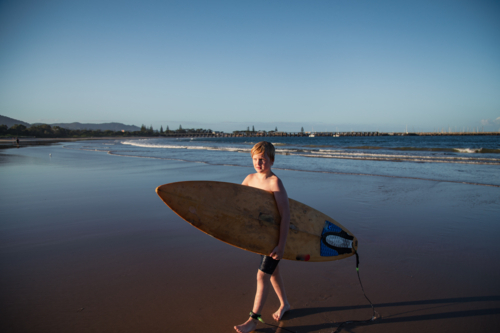 Pre-teen boy carrying surf board out of the water on the beach at Coffs Harbour - Australian Stock Image