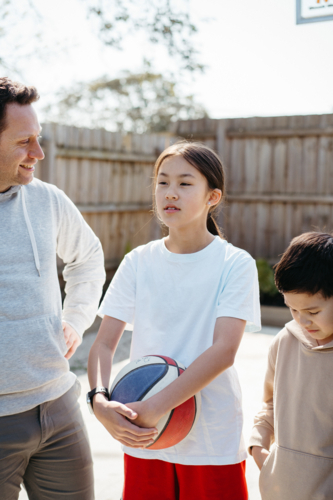 Pre-teen girl holding a ball outdoors with her dad and brother - Australian Stock Image