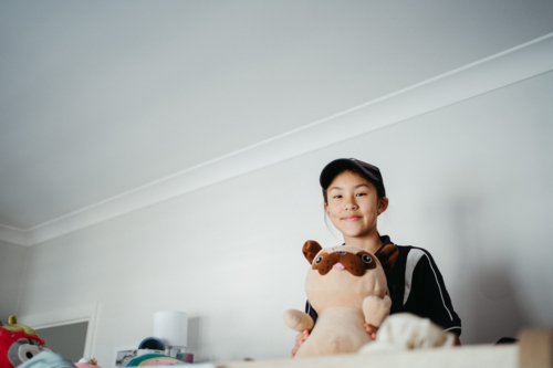 Pre-teen girl sitting on top of the bunk bed holding a plush toy. - Australian Stock Image