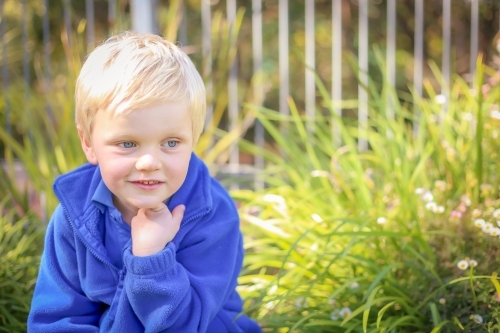 Preschooler sitting in garden with happy expression - Australian Stock Image