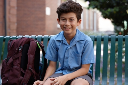 Primary school student at sitting with backpack smiling at camera - Australian Stock Image