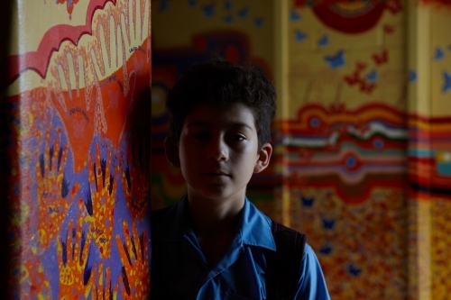 Serious primary school student in shadows of corridor with murals at school - Australian Stock Image