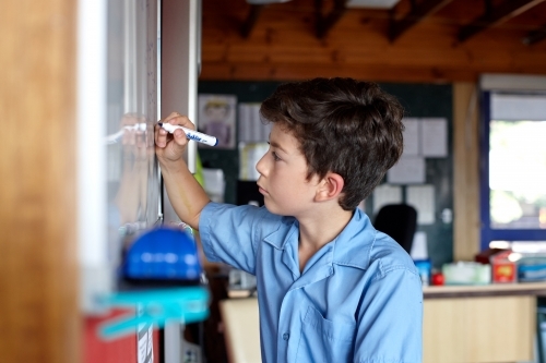 Primary school student in classroom writing on class whiteboard - Australian Stock Image