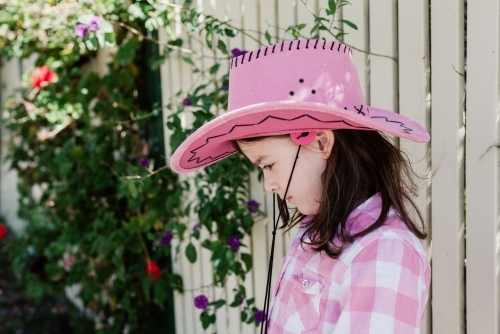 Profile of happy young girl dressed up as a cowgirl wearing a pink akubra hat and pink check shirt - Australian Stock Image