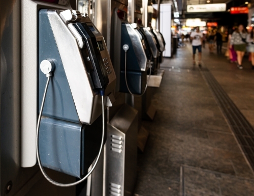 Public phones in city mall with people blurred in background - Australian Stock Image