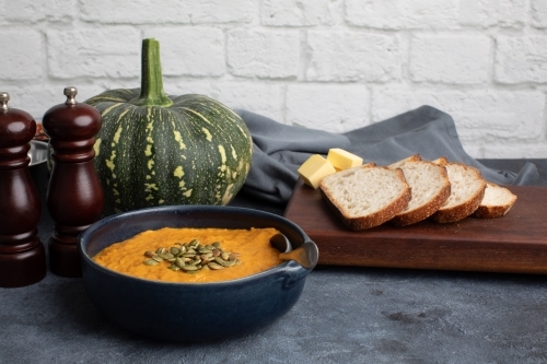 Pumpkin soup scene on dark blue kitchen bench with whole pumpkin - Australian Stock Image