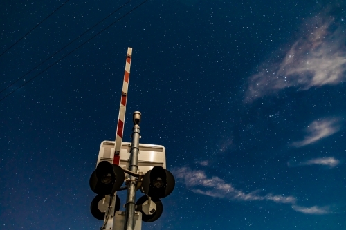 Rail crossing signals and boom barrier against the starry cloudy night sky