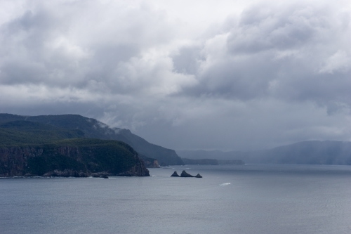 Rain and clouds over headland and island in a sombre coastal setting - Australian Stock Image