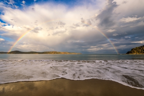 Rainbow over ocean and sandy beach - Australian Stock Image