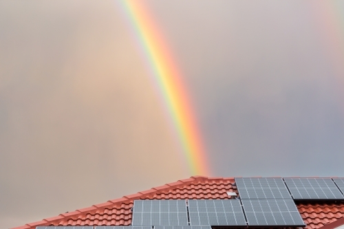 Rainbow over roof of house with solar panels shining after rain storm - Australian Stock Image