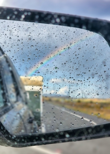 Raindrops on side mirror of car with view of caravan and rainbow - Australian Stock Image