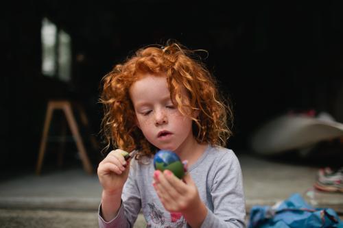 Red haired girl painting easter eggs - Australian Stock Image