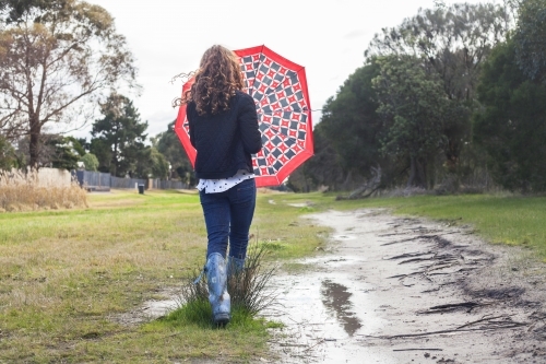 Red haired girl splashing in puddles in gumboots on a rainy winter day. - Australian Stock Image