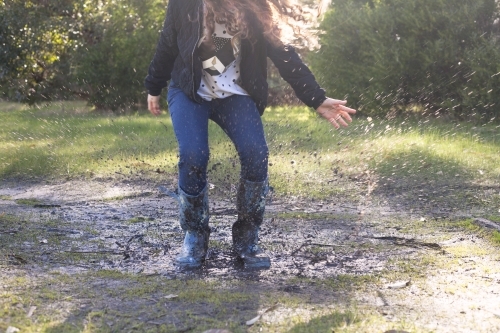 Red haired girl splashing in puddles in gumboots on a rainy winter day.