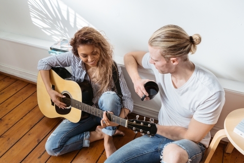 Relaxed couple enjoying playing guitar at home - Australian Stock Image