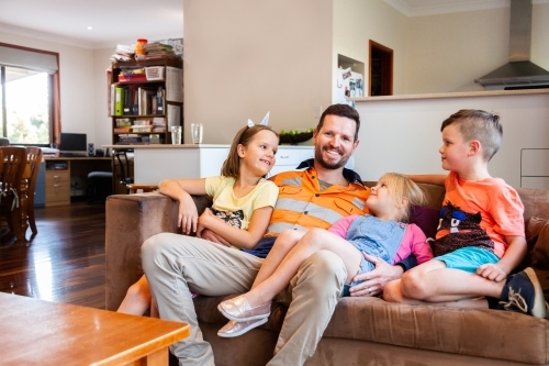 Relaxed tradie hanging out with his kids on lounge - Australian Stock Image