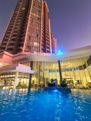 Resort swimming pool at high rise hotel illuminated at night - Australian Stock Image