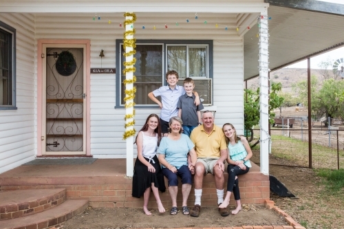 Retired grandparents sitting on front verandah of house with grandchildren happy