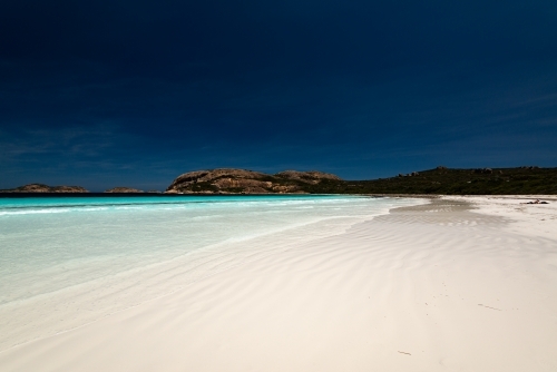 Rippling wave patterns on a white sand beach with beautiful clear shore line and deep blue polarised - Australian Stock Image