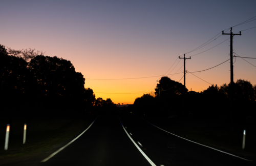 Road at evening after sunset with silhouette of powerlines and tree - Australian Stock Image