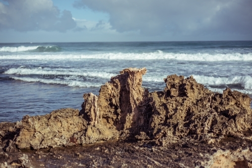 Rock formation on coast with crashing waves on overcast day - Australian Stock Image