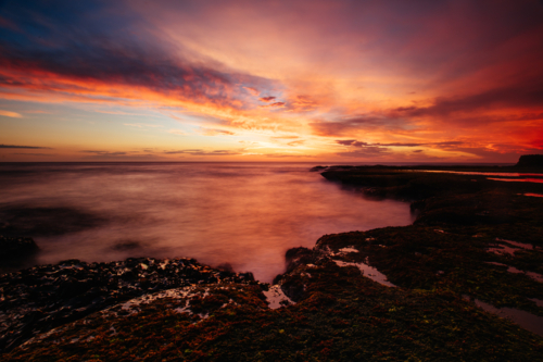 rocks and smooth water of Pearses Beach around Pirates Bay Cove on a hot summer's evening - Australian Stock Image