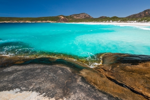 Rocky foreground with clear water and sweeping view of coastline with white sand beach - Australian Stock Image