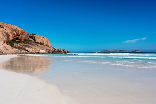 rocky outcrop at end of white sandy beach under blue sky - Australian Stock Image