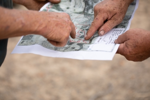 rough workers hands pointing to red line on map - Australian Stock Image