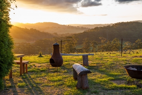 Rural setting at sunset with fireplace and seating overlooking a valley and mountain range - Australian Stock Image