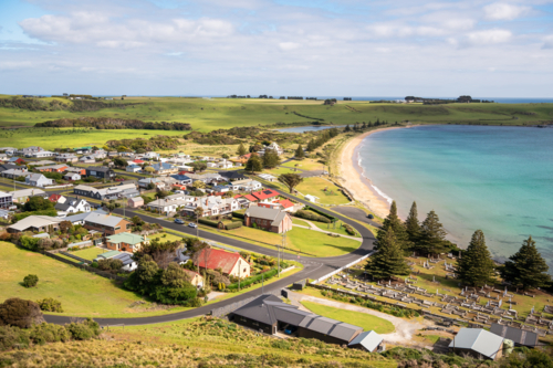 Rural valley landscape with farm buildings and hills in the distance along the shore - Australian Stock Image