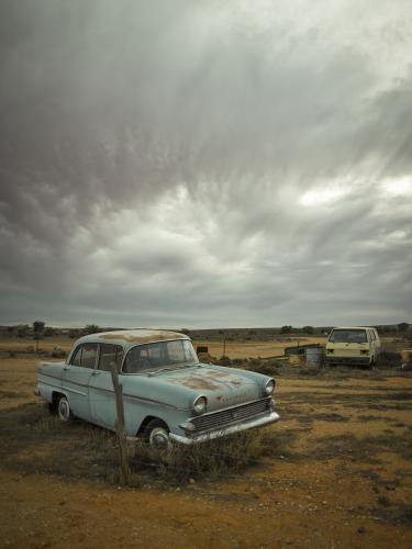 Rusted out blue car in the outback against dramatic sky - Australian Stock Image