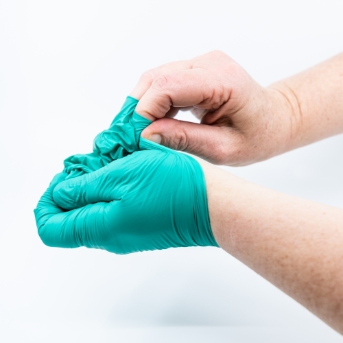 Safely removing green surgical gloves - Australian Stock Image