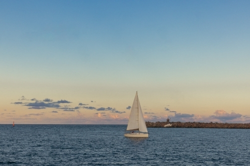 Sail boat entering the Hunter River past the Nobby's Beach breakwall at Newcastle, NSW - Australian Stock Image