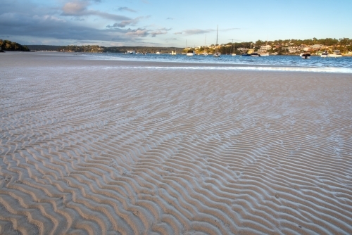 Sand flat with sinusoidal ripples in foreground and houses in the background - Australian Stock Image