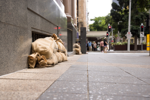 Sandbags along the footpath lining the lower windows of a building in Brisbane CBD before a cyclone - Australian Stock Image