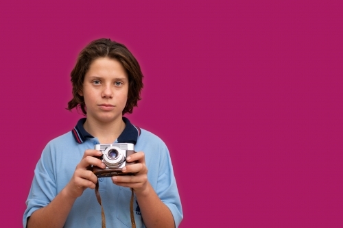 schoolboy holding vintage camera in front of magenta background - Australian Stock Image
