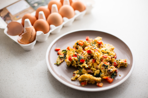 scrambled eggs with veggies next to an egg carton - Australian Stock Image