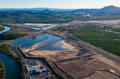 Sedimentation ponds at Wiggins Island Coal Export Terminal (Wicet) with industrial sites and hills. - Australian Stock Image