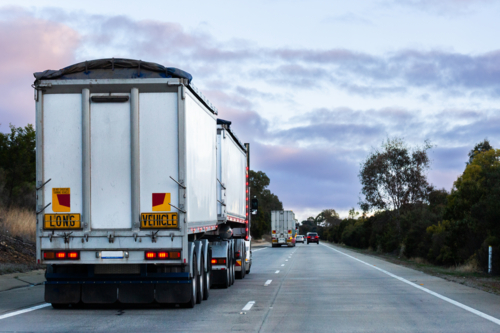 Semi trailer truck transporting goods down rural highway at dusk - Australian Stock Image