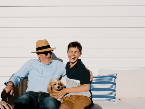 Senior man sitting with a young boy and small dog on the couch. - Australian Stock Image